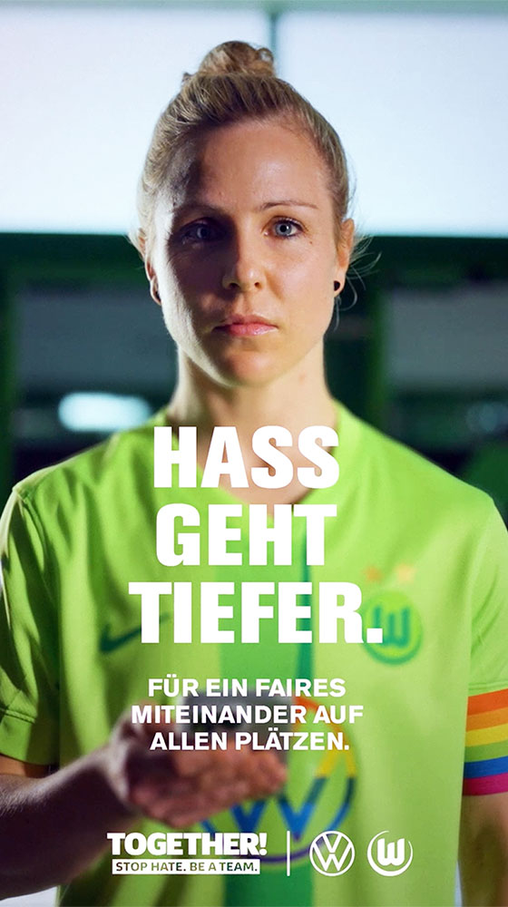 VfL-Wolfsburg-Spielerin Svenja Huth im Vielfaltstrikot mit einem Handy in der Hand. Vor ihr der Text "Hass geht tiefer. Für ein faires Miteinander auf allen Plätzen."