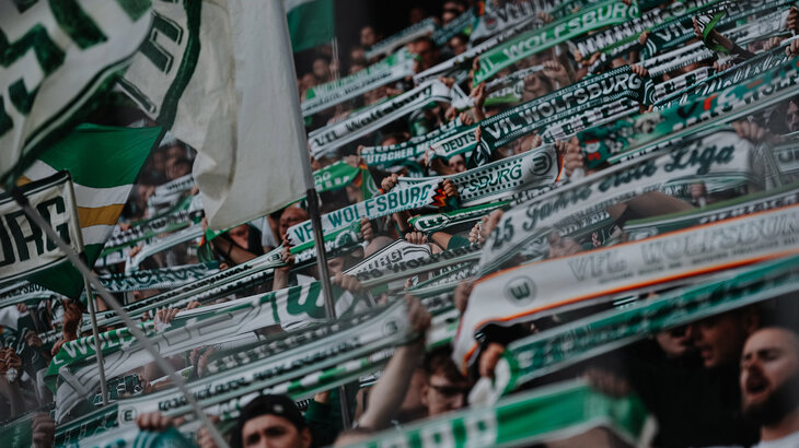 Fans des VfL Wolfsburg halten grün-weiße Schlas in die Höhe.