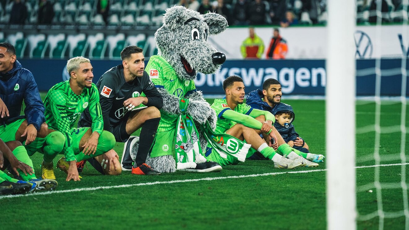 Die VfL-Wolfsburg-Spieler Koen Casteels und Paulo Otavio mit dem Maskottchen Wölfi vor der Fankurve.
