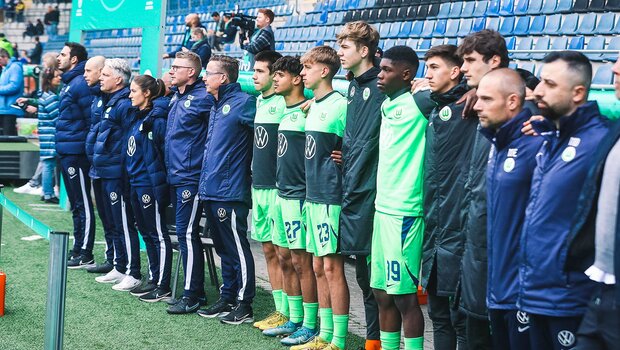 Trainer, Ersatzspieler und Betreuer der U17-Mannschaft des VfL Wolfsburg stehen Arm in Arm am Spielfeldrand.