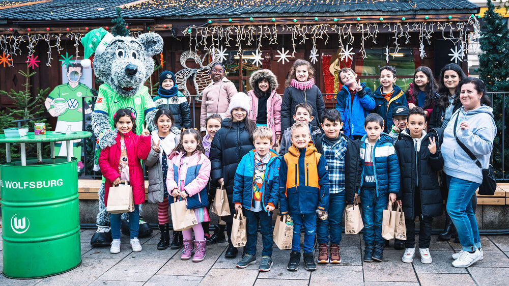Kinder machen ein Bild mit Wölfi auf dem Weihnachtsmarkt.