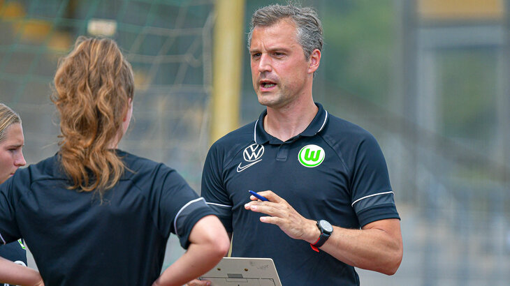 VfL-Wolfsburg-Trainer Daniel Kraus hält ein Tablet in der Hand und gibt den Spielerinnen Anweisungen.