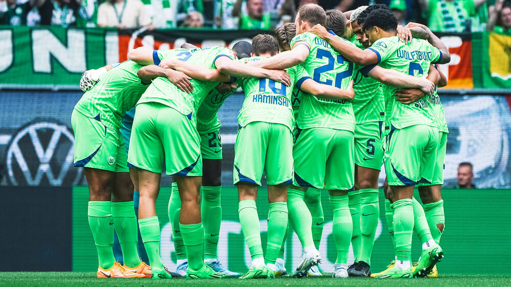 Die Herrenmannschaft des VfL Wolfsburg steht im Kreis Arm in Arm auf dem Spielfeld.