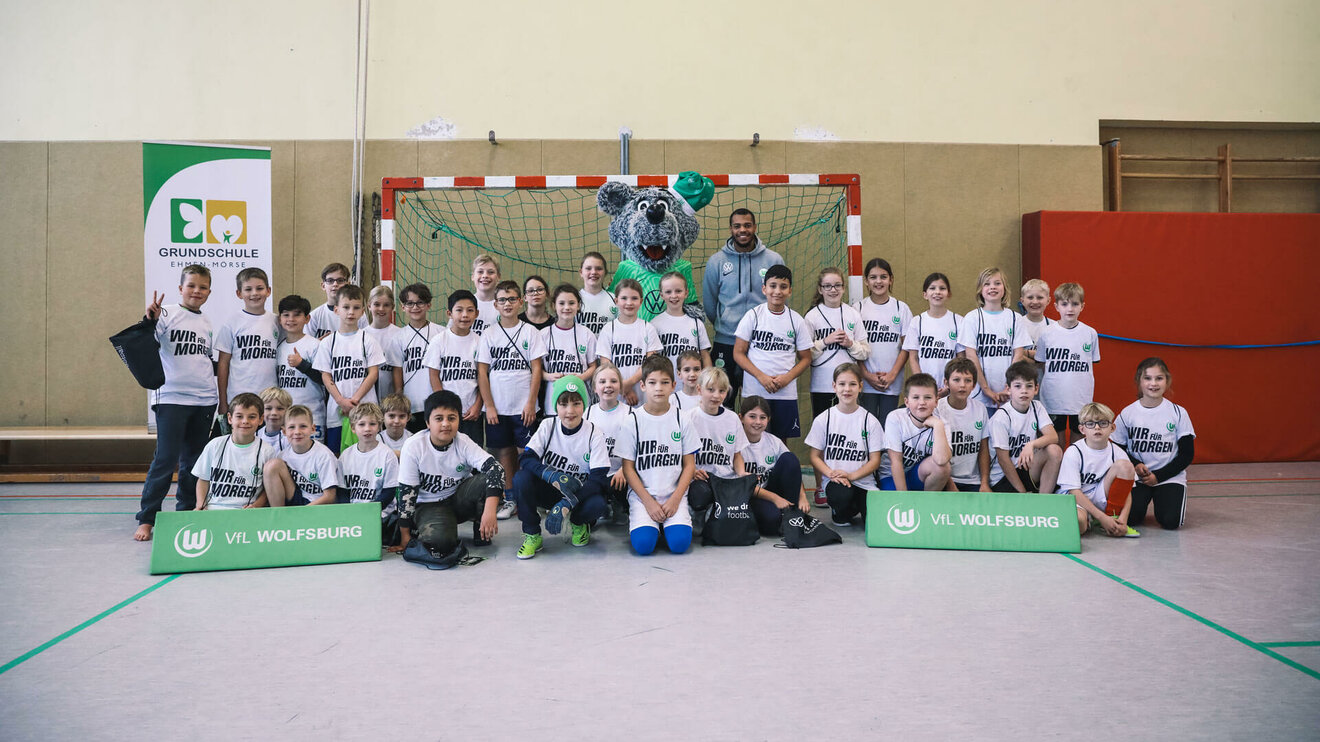 Ein Gruppenbild mit VfL Wolfsburg-Stürmer Lukas Nmecha und den Kindern der "Wir für morgen"-Schule.