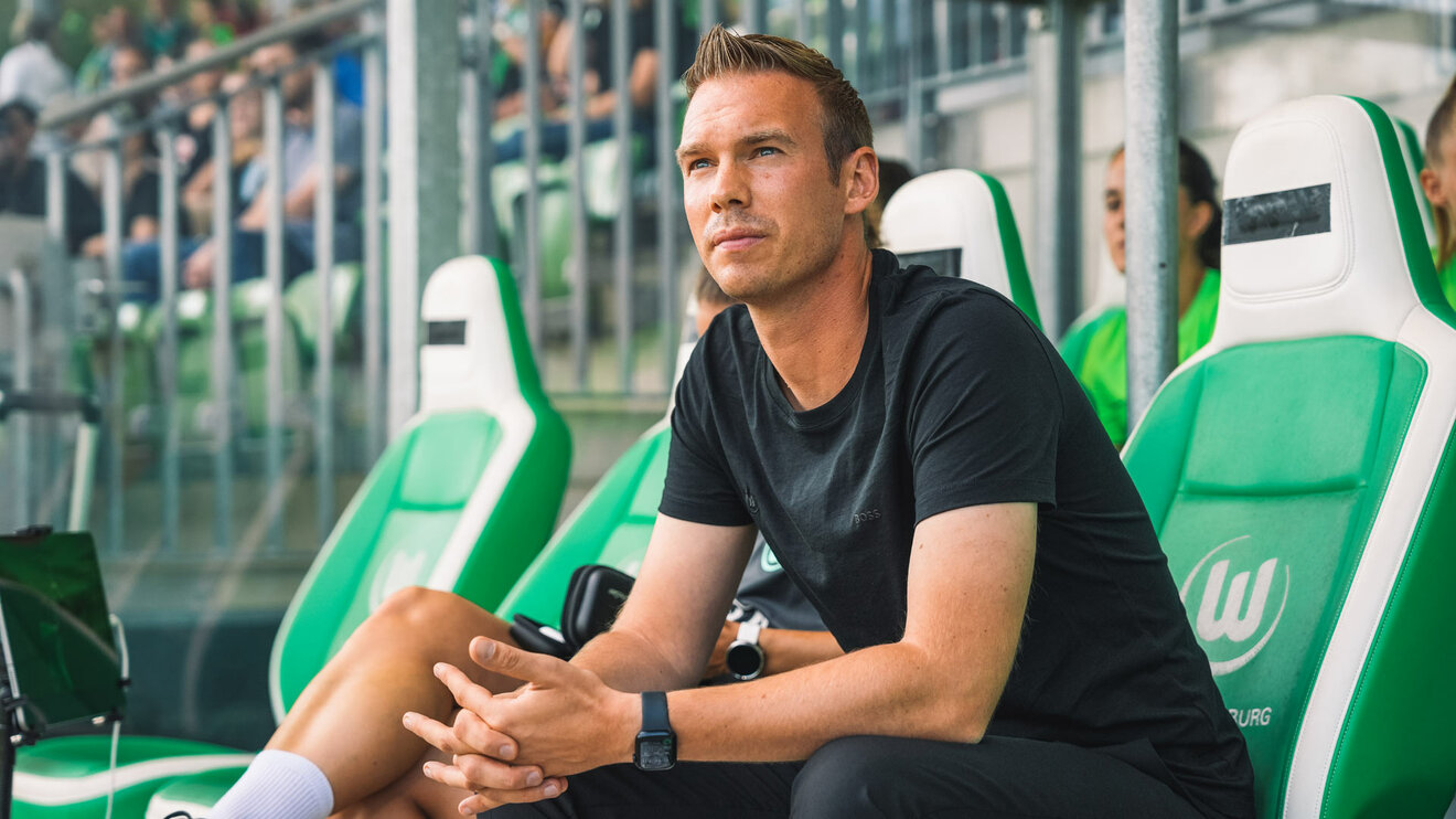 Der VfL Wolfsburg Trainer Tommy Stroot schaut von der Trainerbank auf das Spielfeld.