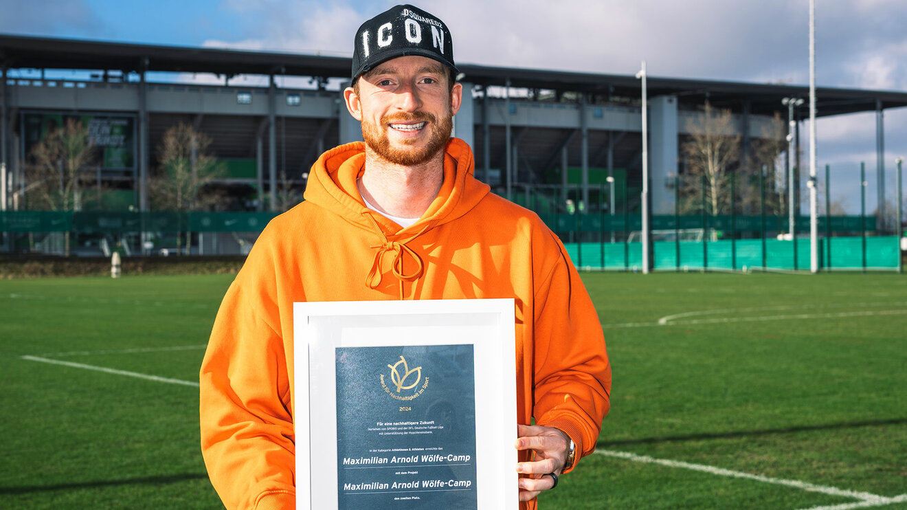 VfL Wolfsburg Spieler Max Arnold zeigt seine Auszeichnung in die Kamera.