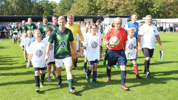 Das Traditionsteam des VfL Wolfsburg läuft mit den Einlaufkindern auf das Feld.