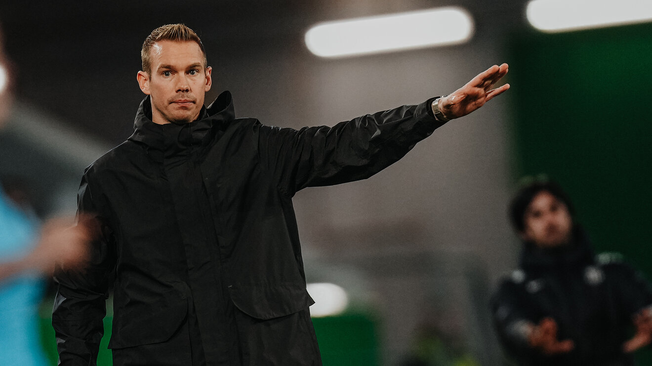 Der VfL-Wolfsburg-Trainer Tommy Stroot hebt eine Hand.