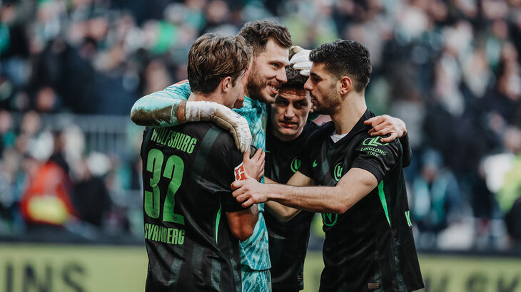 VfL-Wolfsburg-Spieler Marius Müller lächelt und wird von seinen Mitspielern umarmt.