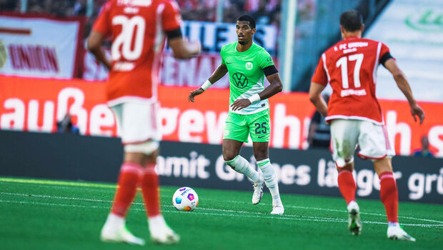 Moritz Jenz vom VfL Wolfsburg schaut nach einer Lücke zwischen den Gegenspielern.
