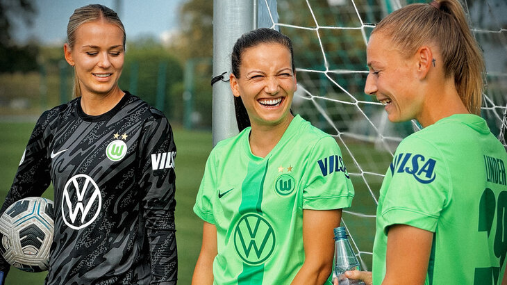 Die VfL Wolfsburg-Spielerinnen Merle Frohms, Joelle Wedemeyer und Sarai Linder stehen lachend vor dem Tor.