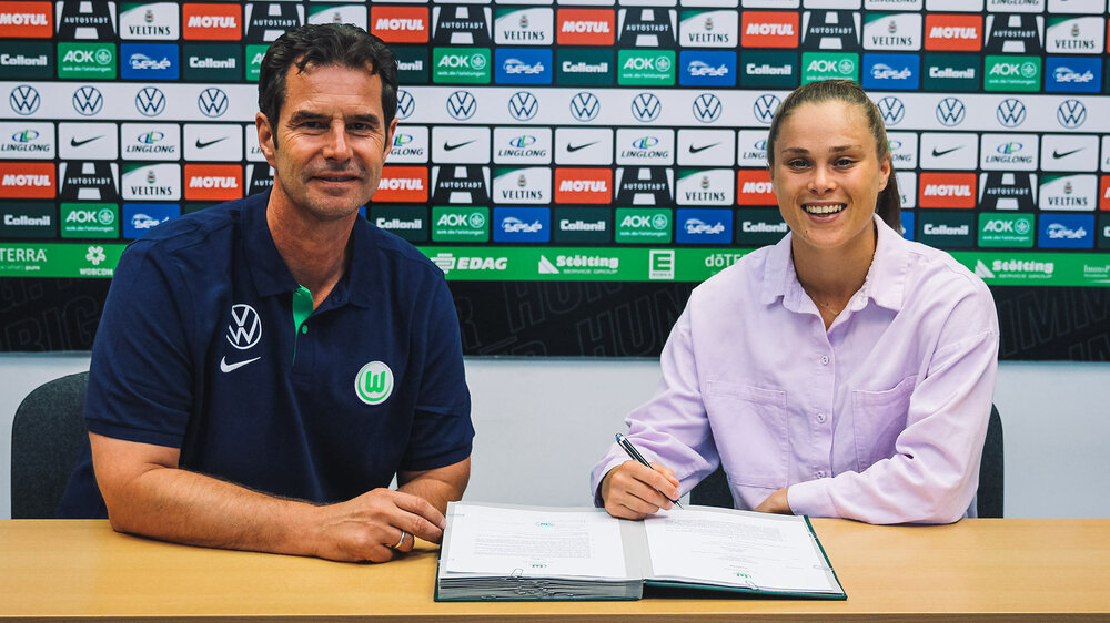 Die VfL Wolfsburg-Spielerin Ewa Pajor lacht bei der Vertragsverlängerung in die Kamera. Neben ihr sitzt Ralf Kellermann.