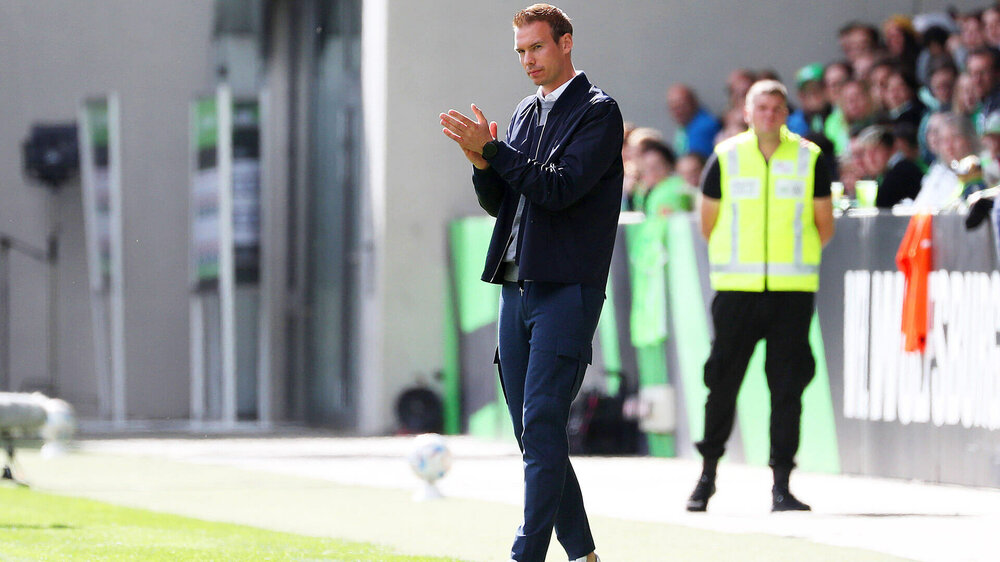 Tommy Stroot, Trainer des VfL Wolfsburg, steht an der Seitenlinie und klatscht in die Hände.