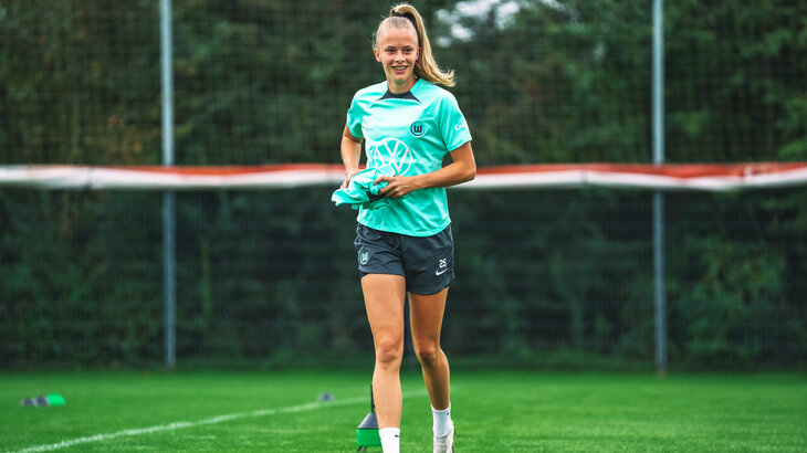 Vivien Endemann vom VfL Wolfsburg hält ein Trainingsshirt in den Händen und läuft über den Platz.