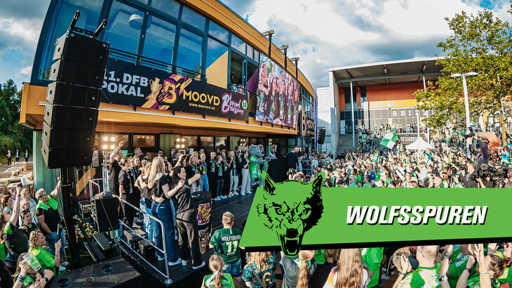Fans des VfL Wolfsburg feiern die Frauenmannschaft, die auf einer Bühne steht, an einem sonnigen Tag vor der B'moovd Sportsbar.