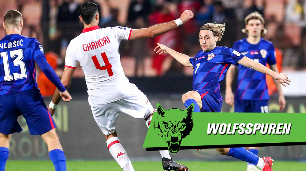 Der VfL-Wolfsburg-Spieler Lovro Majer im kroatischen Nationaltrikot versucht, den Ball zu erobern. Davor befindet sich der Schriftzug "Wolfsspuren".
