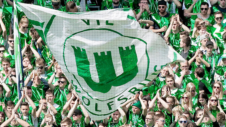 Inmitten der Wölfe-Fans wird eine Fahne vom VfL Wolfsburg geschwenkt.