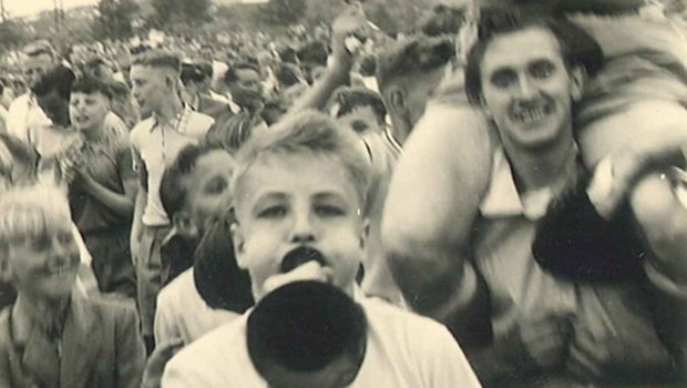 Ein historisches Fanbild des VfL Wolfsburg. Ein Fan bläst in eine Tröte. 