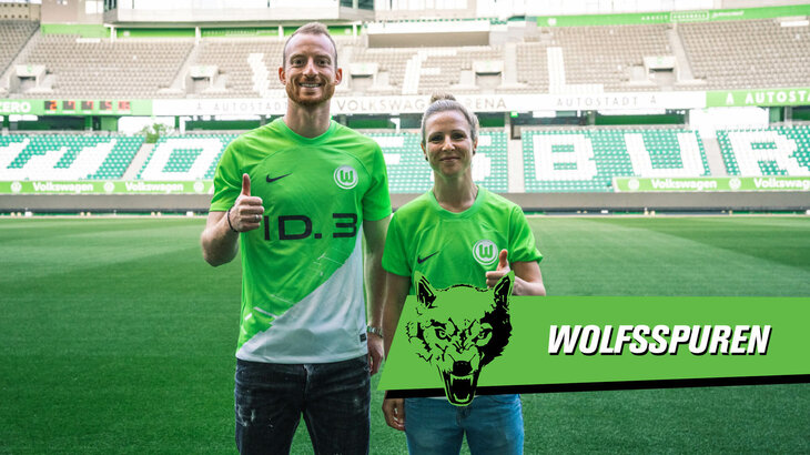 VfL Wolfsburg Spieler Arnold und Spielerin Huth posieren im neuen Heimtrikot in der Volkswagen Arena und halten einen Daumen hoch.