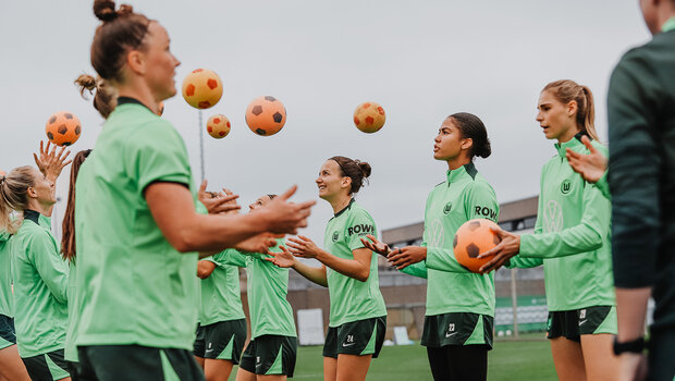 Die VfL-Wolfsburg-Spielerinnen stehen sich in zwei Reihen gegenüber und werfen sich Bälle zu. 