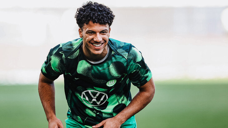 U19-Kapitän vom VfL-Wolfsburg Jonathan Akaegbobi auf dem Platz im VfL Trikot, wie er in die Kamera lacht.