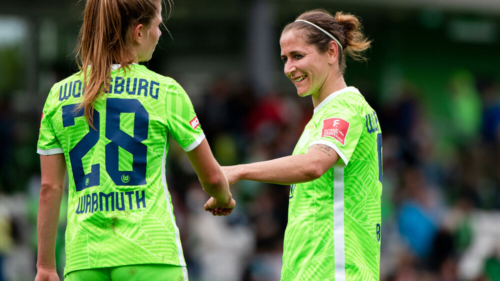Die VfL Wolfsburg Spielerinnen Anna Blässe und Tabea Waßmuth lächeln zueinander.