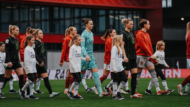 Die Spielerinnen des VfL Wolfsburg laufen neben den Spielerinnen des FC Bayern gemeinsam mit den Einlaufkindern auf das Spielfeld.
