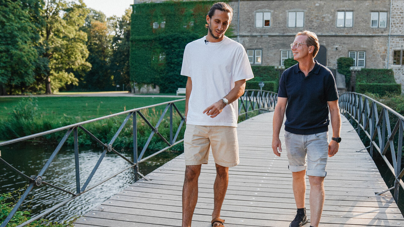 Der VfL-Wolfsburg-Spieler Kamil Grabara und Roy Präger schauen sich an, während sie über eine Brücke gehen.