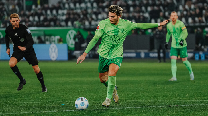 VfL Wolfsburg Spieler Jonas Wind holt aus um den Ball über den Platz zu schießen.