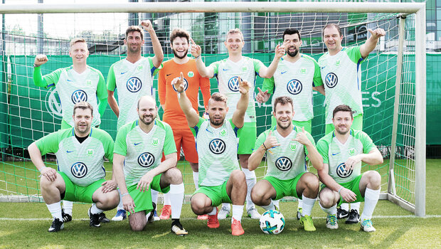 Business-Partner posieren im Dress des VfL Wolfsburg als Mannschaft in einem Tor.