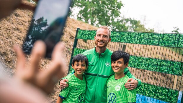 Zwei Jungen aus dem Maximilian Arnold Wölfe Camp machen ein Foto mit dem VfL Wolfsburg Kapitän in der Mitte.