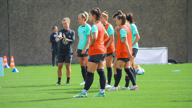 Die Spielerinnen des VfL Wolfsburg stehen auf dem Trainingsplatz und beobachten das Spiel.
