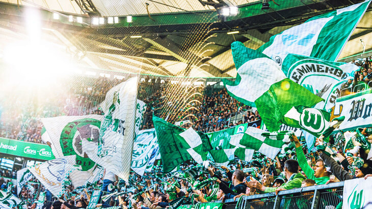 Die Fans des VfL Wolfsburg wedeln mit ihren Fahnen und Schals in der Volkswagen Arena.