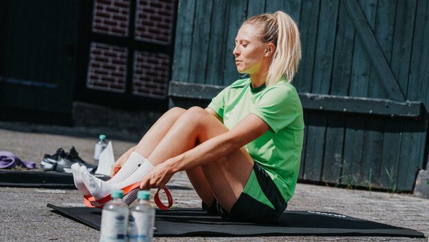 Die VfL-Wolfsburg-Spielerin Rebecka Blomqvist sitzt auf einer Matte mit angewinkelten Beinen.