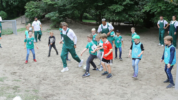 VfL Wolfsburg Spieler kicken in Latzhosen mit Kindern im Rahmen des "Wir für euch"-Tags.