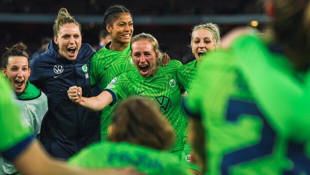 Kim Kulig freut sich mit den Spielerinnen des VfL Wolfsburg und umarmt diese.