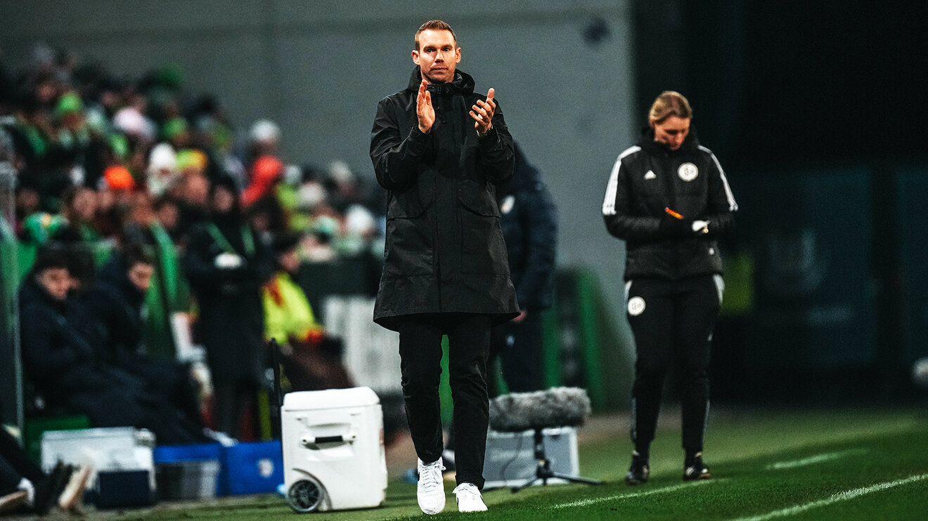 VfL-Wolfsburg-Trainer Tommy Stroot steht an der Seitenlinie und klatscht.