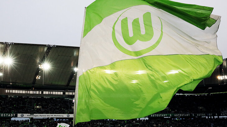 Eine große grün-weiße Fahne mit dem VfL Wolfsburg-Logo weht am Spielfeldrand hin und her.