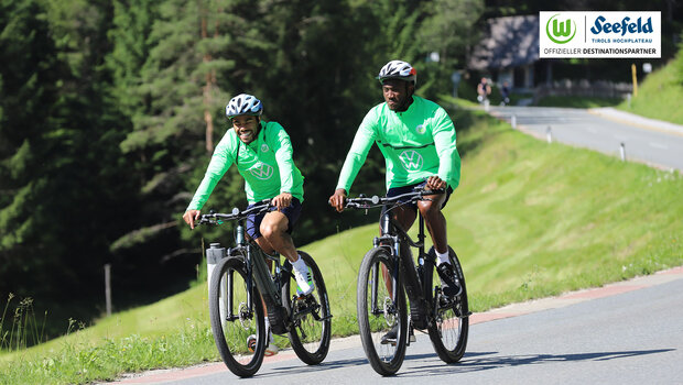 Die VfL Wolfsburg-Spieler Paulo Otavio und Josuha Guilavogui fahren mit dem Fahrrad auf der Straße.