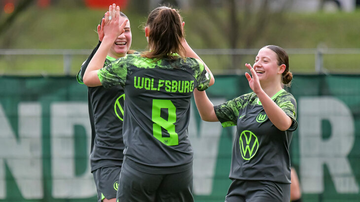Drei Spielerinnen der VfL Wolfsburg U17 Wölfinnen klatschen sich auf dem Spielfeld ab und jubeln.