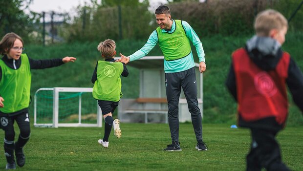 VfL-Wolfsburg-Spieler Mattias Svanberg macht ein High Five mit einem Kind.