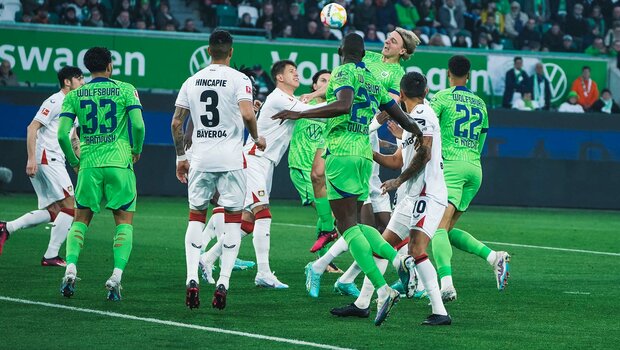Die Spieler des VfL Wolfsburg und Sebastiaan Bornauw springen für einen Kopfball in die Höhe.