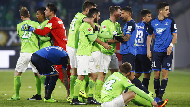 Die VfL Wolfsburg Spieler umarmen sich auf dem Spielfeld, einer sitzt. Neben ihnen stehen Spieler von Hoffenheim.