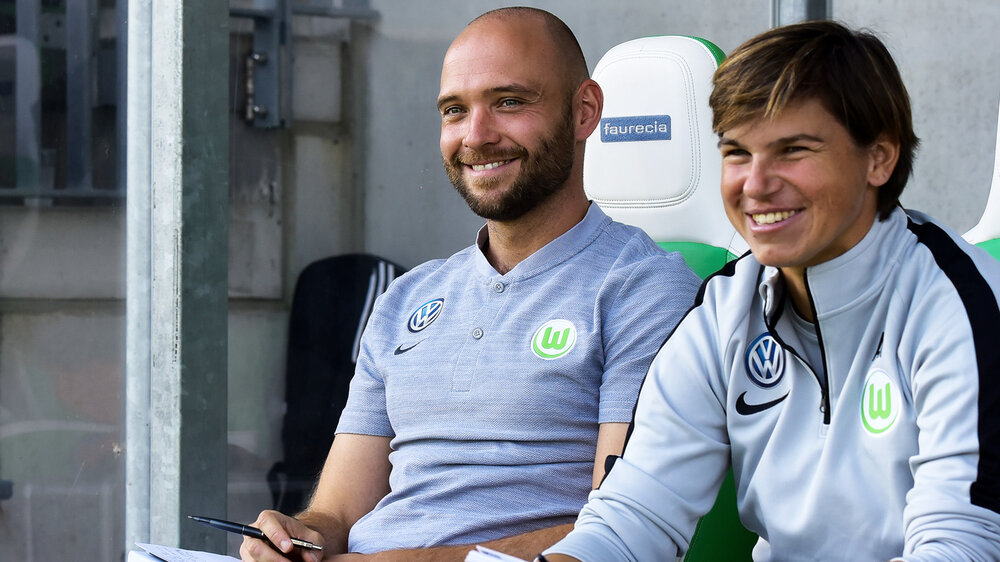 Stephan Lerch und Ariane Hingst lächelnd auf der Trainerbank im AOK Stadion.