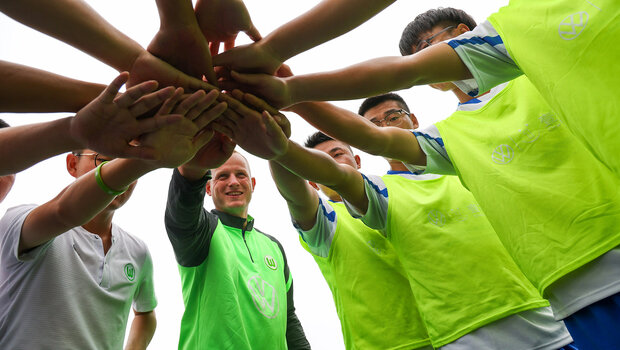 Teilnehmende des Fußballcamps bilden einen Kreis und legen ihre Hände übereinander. 
