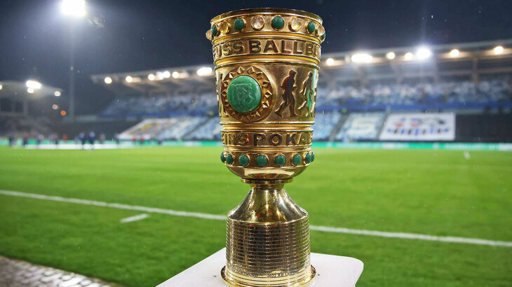 Der DFB-Pokal vor dem Spielfeld bei Nacht.