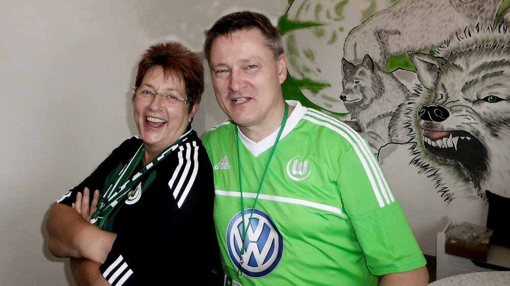 Zwei Mitglieder aus dem Faneck des VfL Wolfsburg umarmen sich in VfL-Trikots.