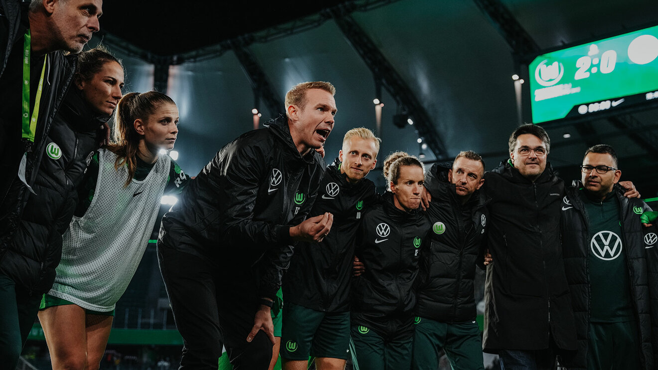 Die komplette Mannschaft der VfL-Wolfsburg-Frauen steht Arm-in-Arm in einem Kreis. Trainer Tommy Stroot hebt sich etwas ab in dem er im Kreis steht und zu ihnen spricht. 