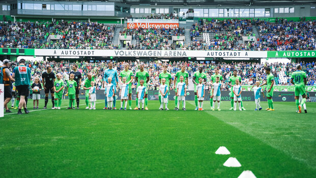 Die Wölfe des VfL Wolfsburg stellen sich vor dem Spiel gegen Schalke mit den Einlaufkindern auf dem Platz auf.