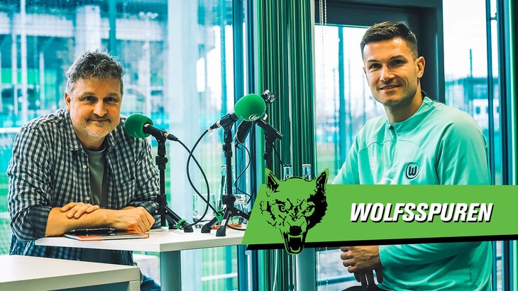 VfL-Wolfsburg-Spieler Pavao Pervan und ein Moderator sitzen vor einem Mikrofon und schauen in die Kamera. Daneben der Schriftzug "Wolfsspur".